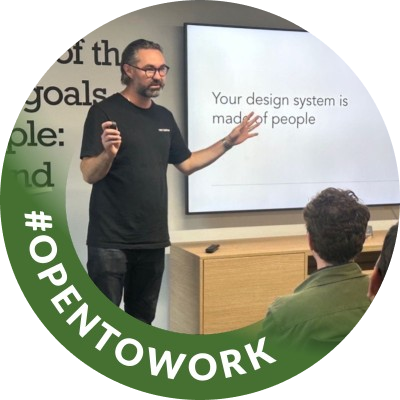 Matt speaking at an event in front of a slide reading &lsquo;Your design system is made of people&rsquo;, with an Open To Work badge